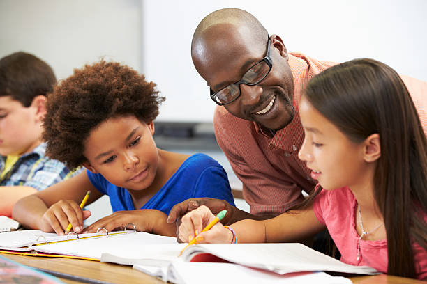 Teacher Helping Pupils Studying At Desks In Classroom Checking Work Smiling Teacher Helping Pupils Studying At Desks In Classroom Checking Work Smiling
